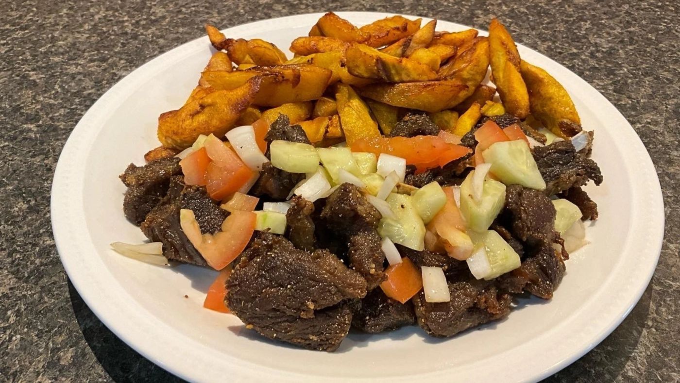 Plate of seared beef pieces topped with diced tomato, cucumber and onion, with fried potatoes