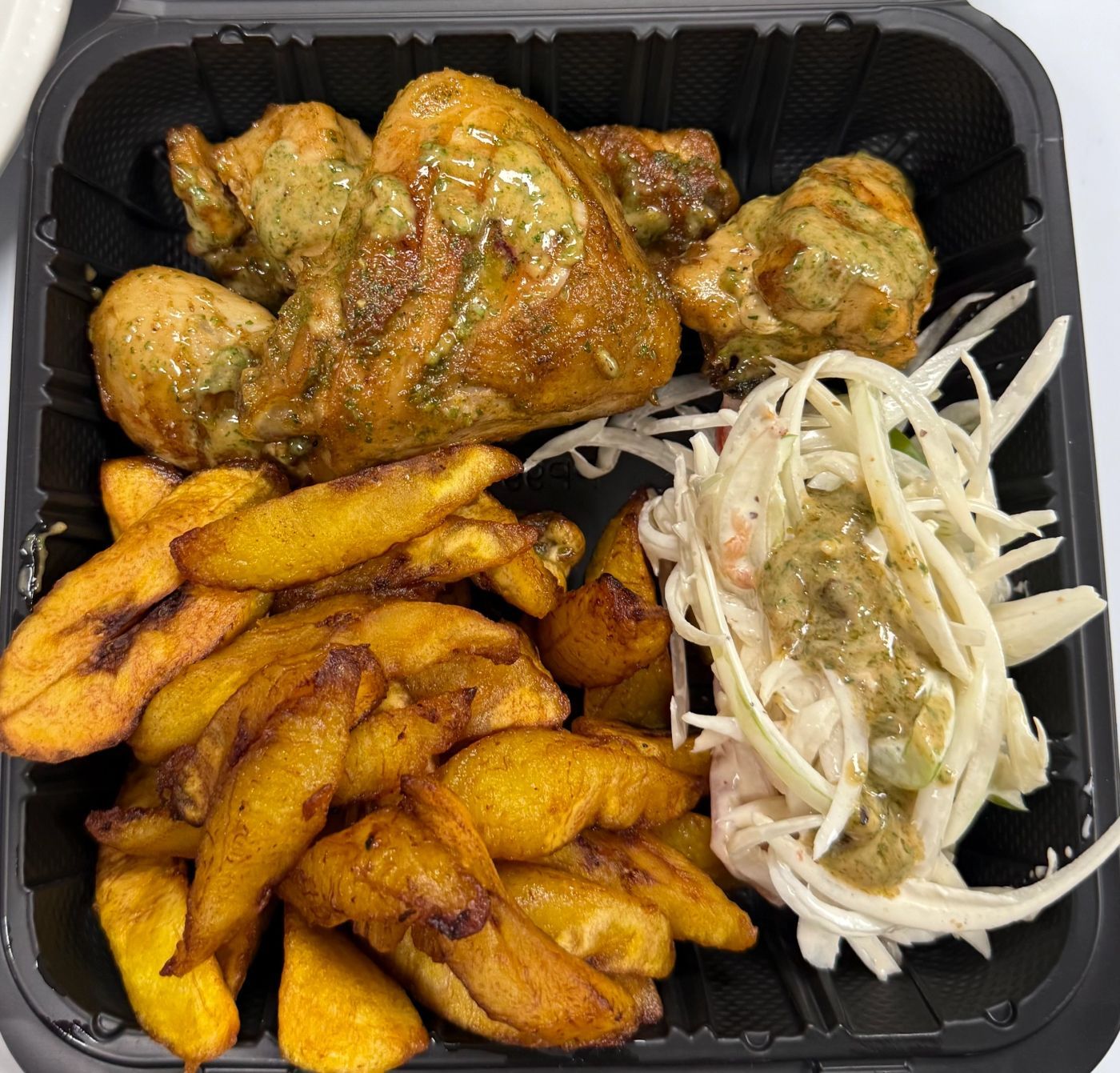 Grilled chicken with fried plantains and cabbage salad in a takeout box