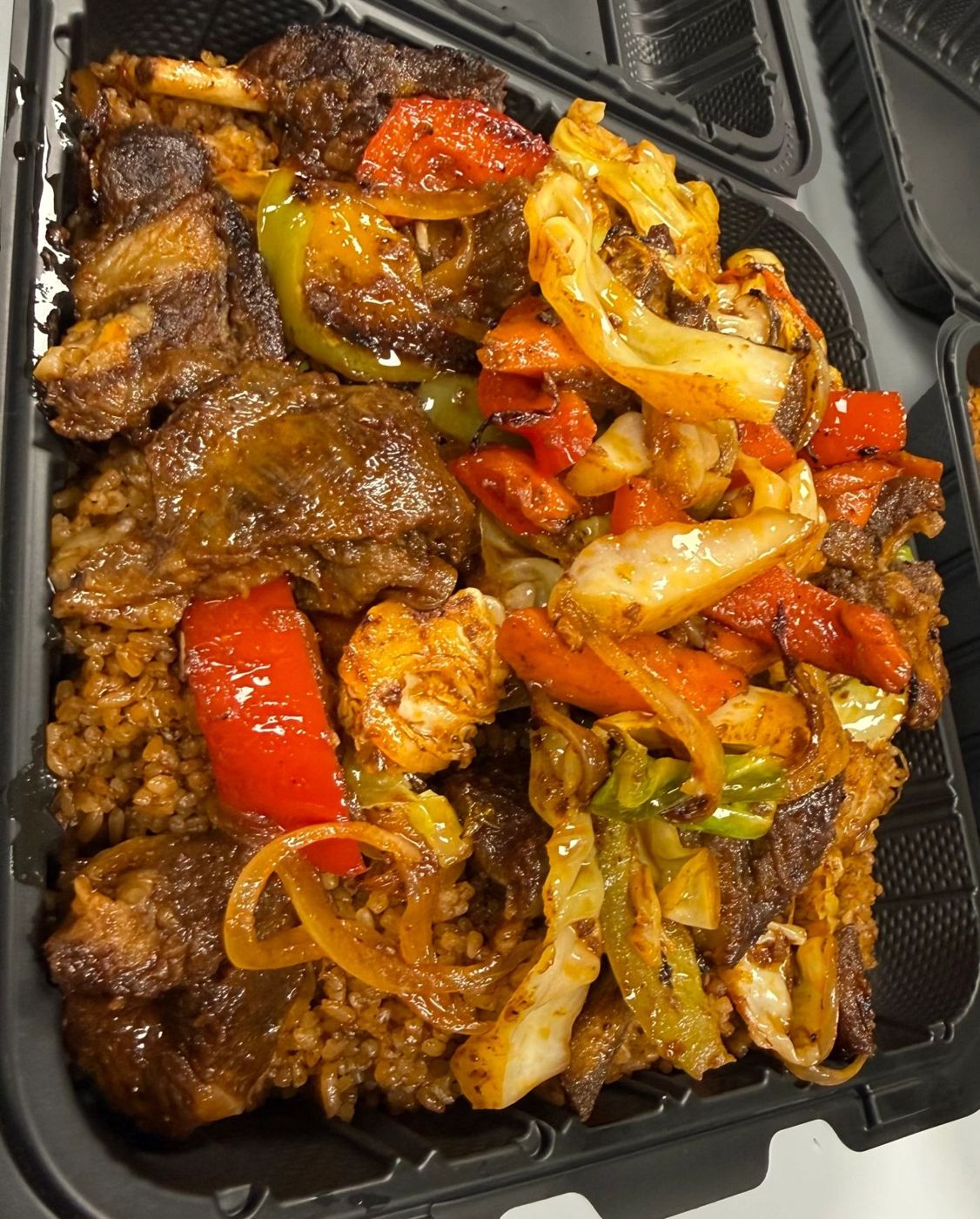 Takeout container of grilled meat with peppers and onions