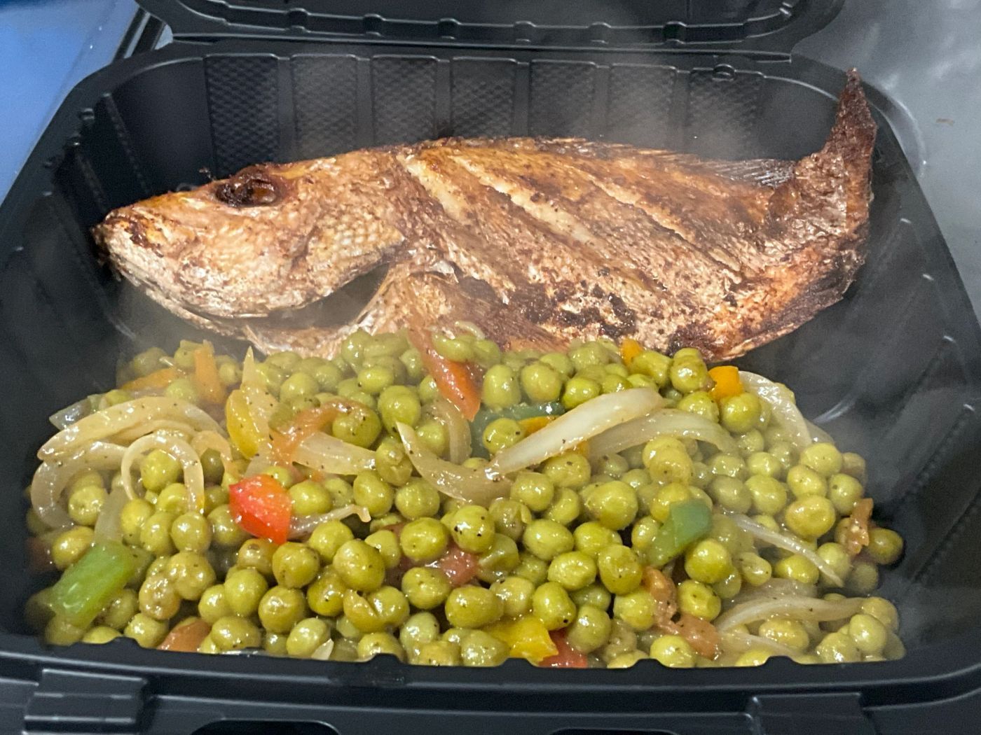 Whole grilled fish over sweet peas with onions in a takeout container
