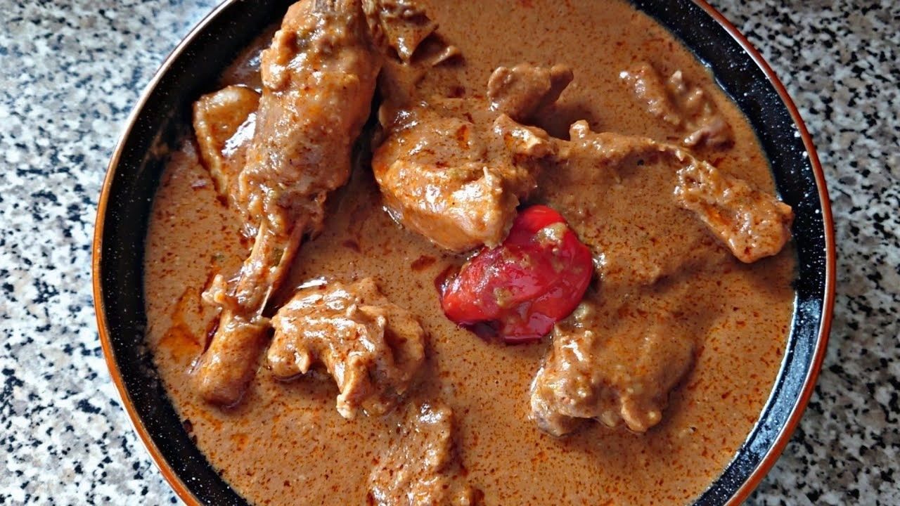 Bowl of rich brown stew with meat and a red pepper
